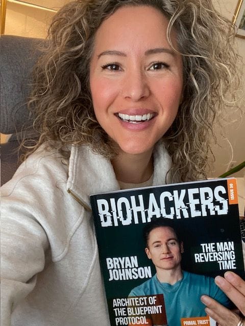 Woman smiling, holding a book titled 'Biohackers.'